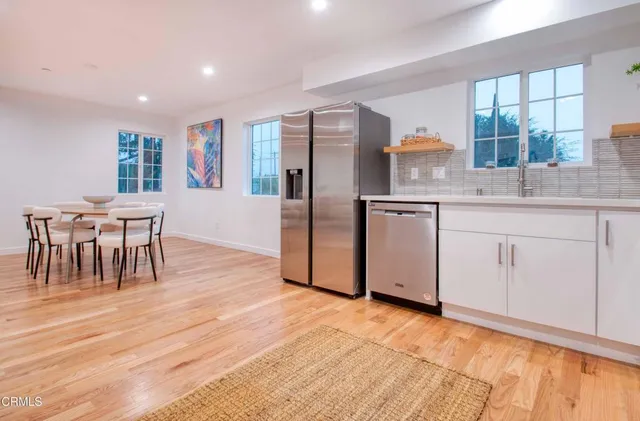 a kitchen with stainless steel appliances granite countertop a stove a sink a refrigerator and white cabinets with wooden floor