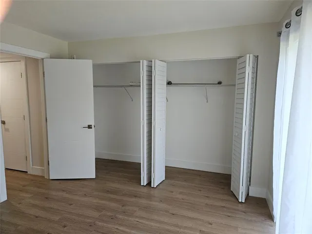a view of an empty room with wooden floor and closet area