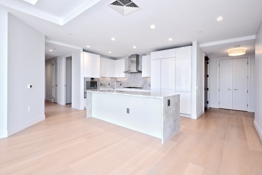135 Seaport Boulevard, Unit PH3A Boston, MA 02210 - Photo 6 of 11 a large white kitchen with stainless steel appliances granite countertop a stove a sink a refrigerator and white cabinets with wooden floor