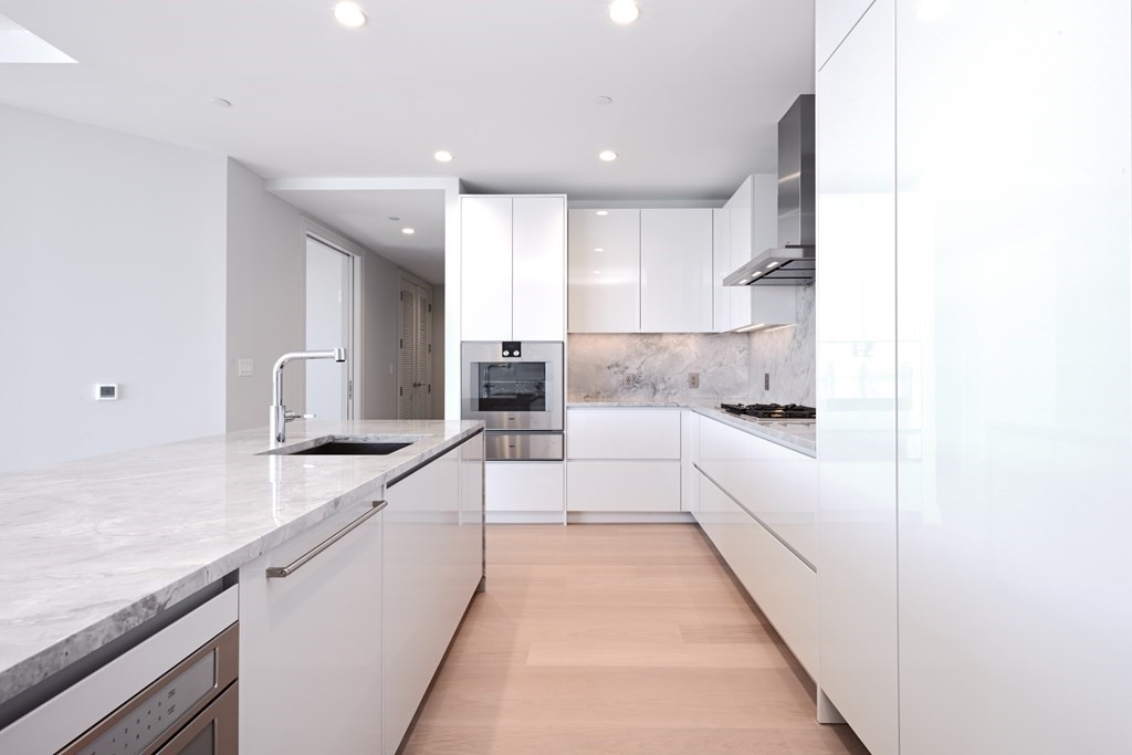 135 Seaport Boulevard, Unit PH3A Boston, MA 02210 - Photo 7 of 11 a large white kitchen with stainless steel appliances kitchen island granite countertop a sink and cabinets