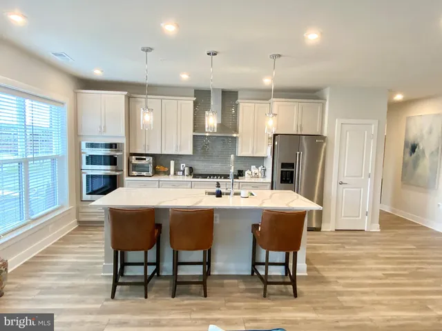 a kitchen with stainless steel appliances granite countertop a dining table chairs refrigerator and cabinets