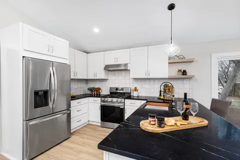 a kitchen with stainless steel appliances granite countertop a sink a stove a refrigerator and white cabinets