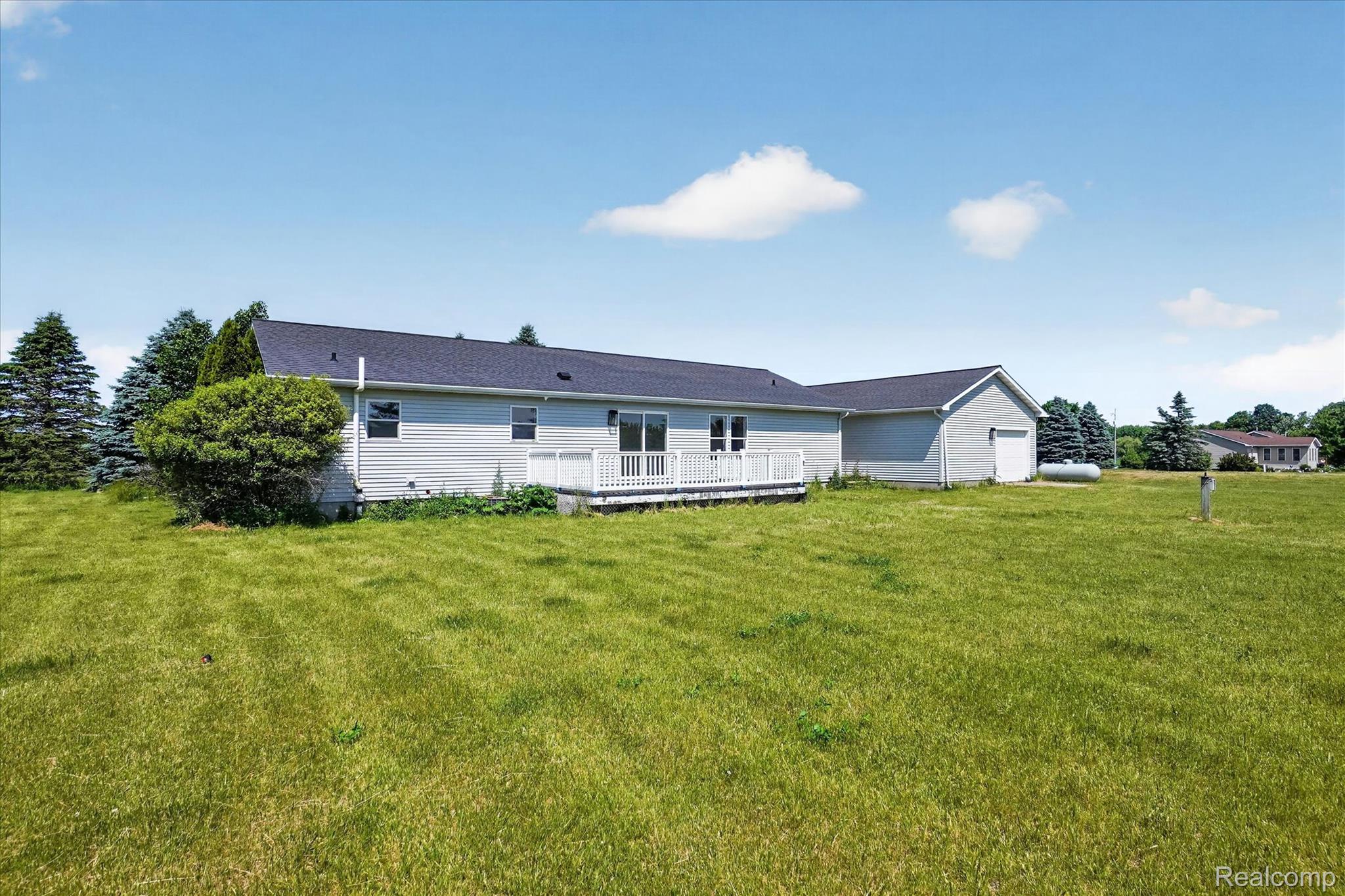 1400 North Every Road Mason, MI 48854 - Photo 28 of 33 Expansive green lawn surrounds a single-story home featuring light grey siding, a dark shingled roof, a white deck, and a detached two-car garage