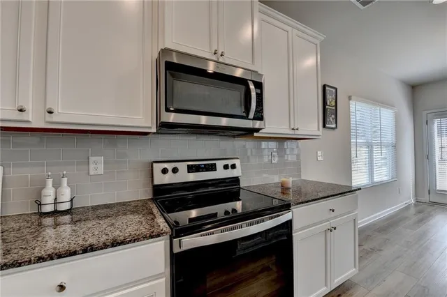 a kitchen with stainless steel appliances granite countertop white cabinets and a stove a sink
