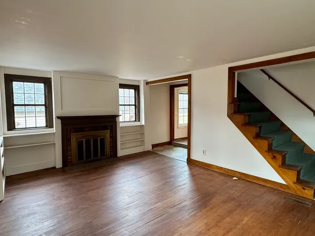 an empty room with wooden floor fireplace and windows