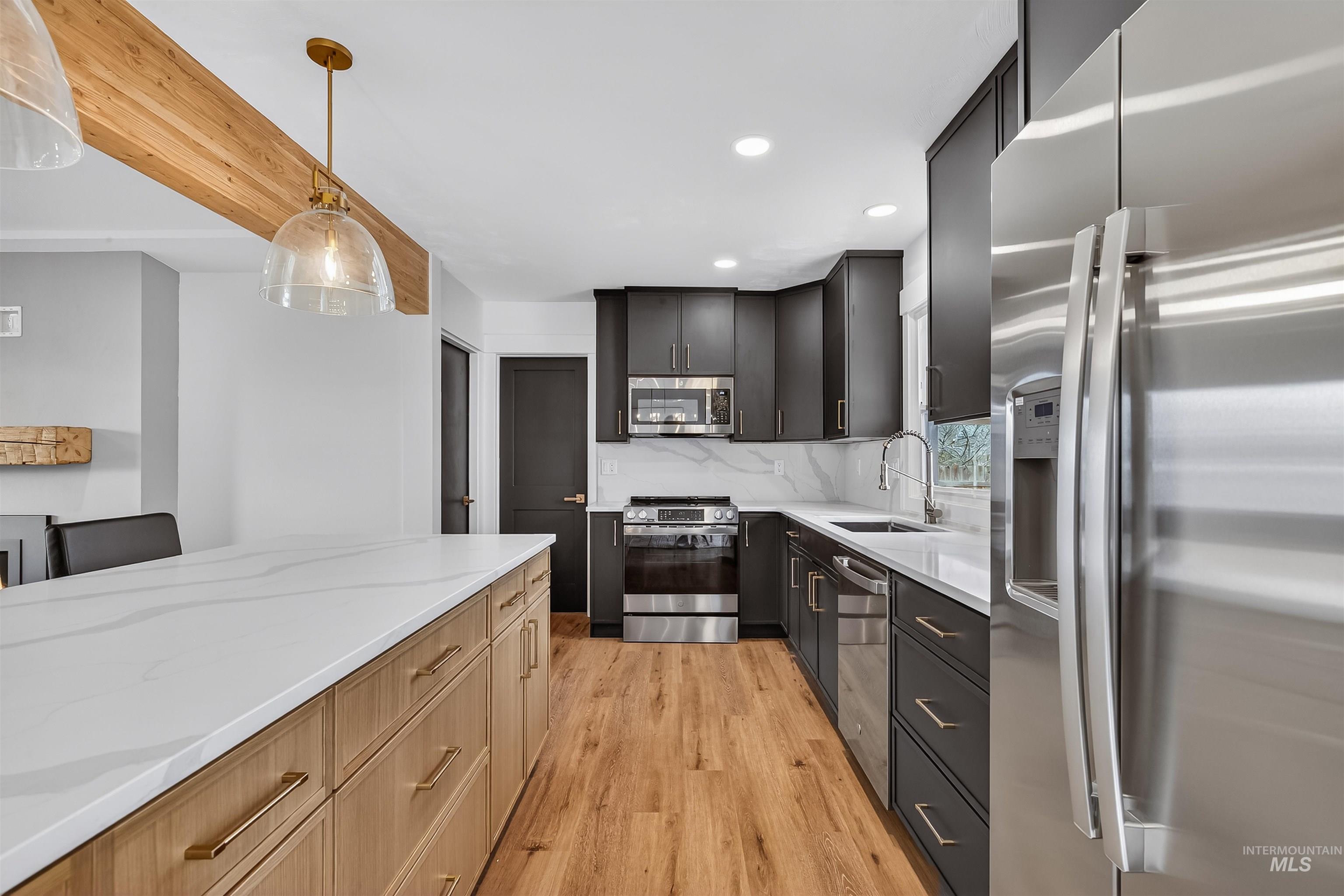 3513 8th Street Lewiston, ID 83501 - Photo 12 of 41 Two tone kitchen with stainless steel appliances, two tone color scheme, light wood-style flooring, light stone countertops, and hanging light fixtures