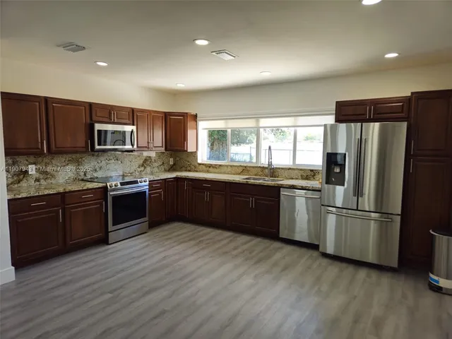 a kitchen with kitchen island granite countertop wooden floors stainless steel appliances and a sink