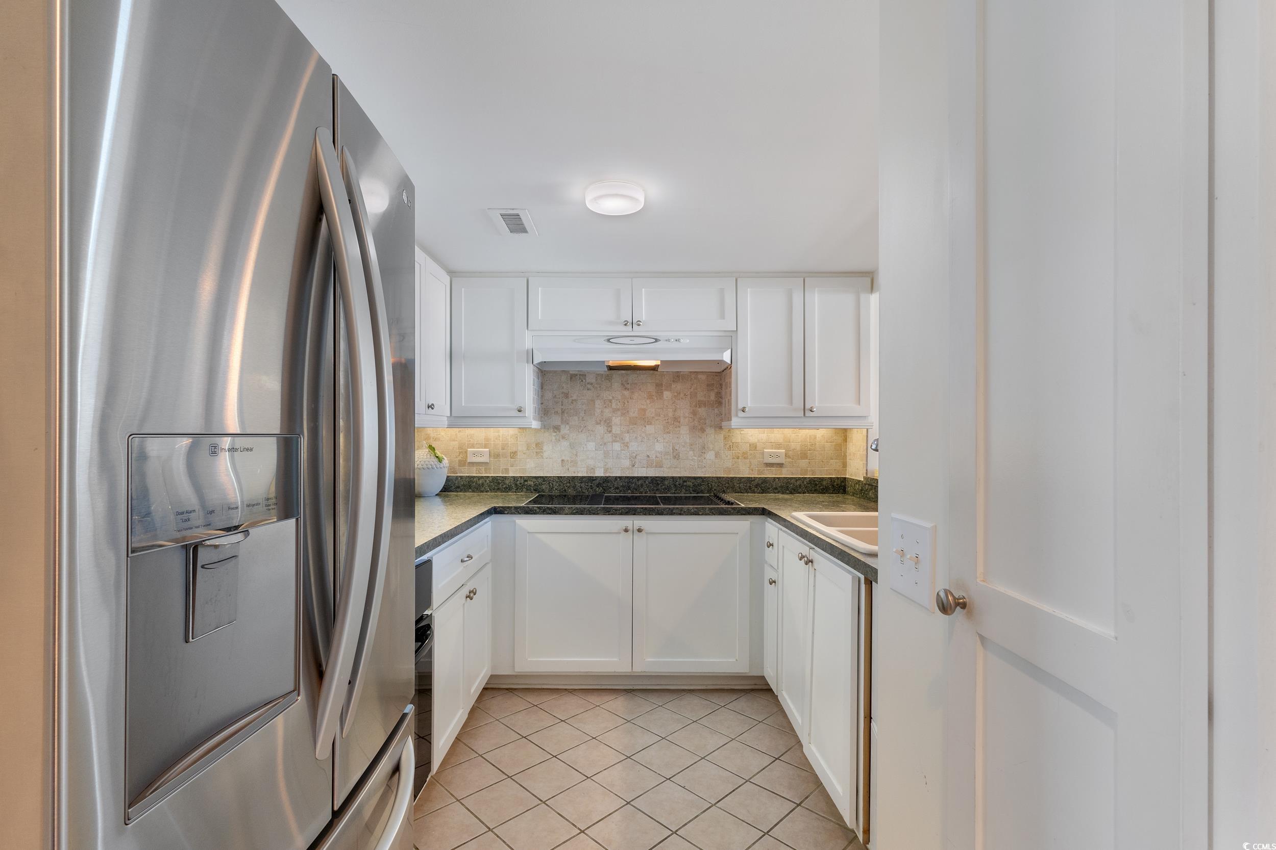 100 Ocean Creek Drive, Unit G14 Myrtle Beach, SC 29572 - Photo 18 of 40 Kitchen with stainless steel fridge with ice dispenser, white cabinetry, tasteful backsplash, and light tile patterned flooring