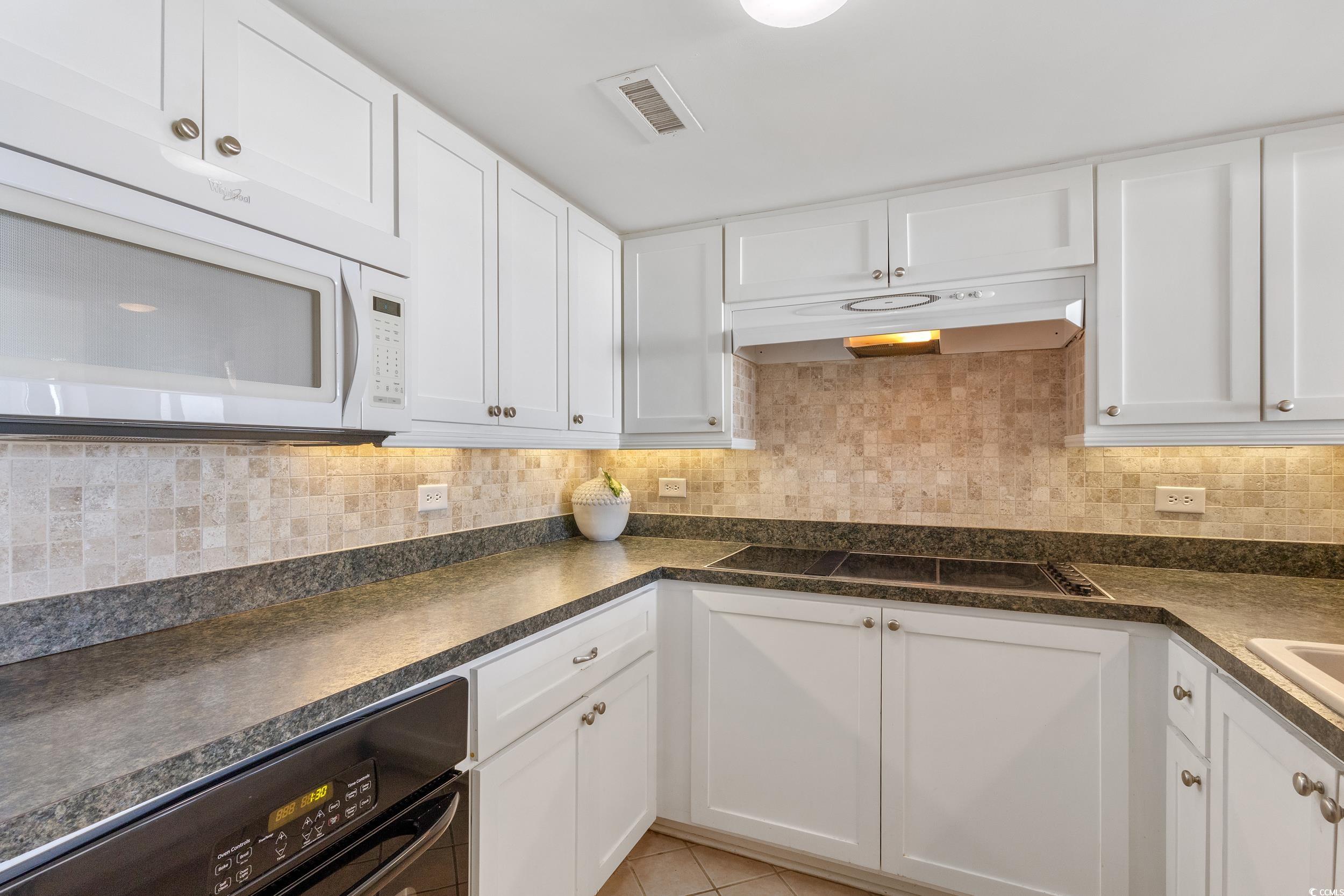 100 Ocean Creek Drive, Unit G14 Myrtle Beach, SC 29572 - Photo 19 of 40 Kitchen with white cabinets, black appliances, under cabinet range hood, dark countertops, and tasteful backsplash