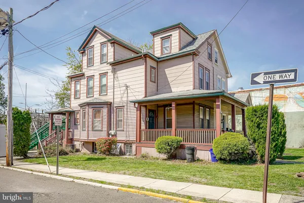 a view of a white house with a yard plants and a large tree