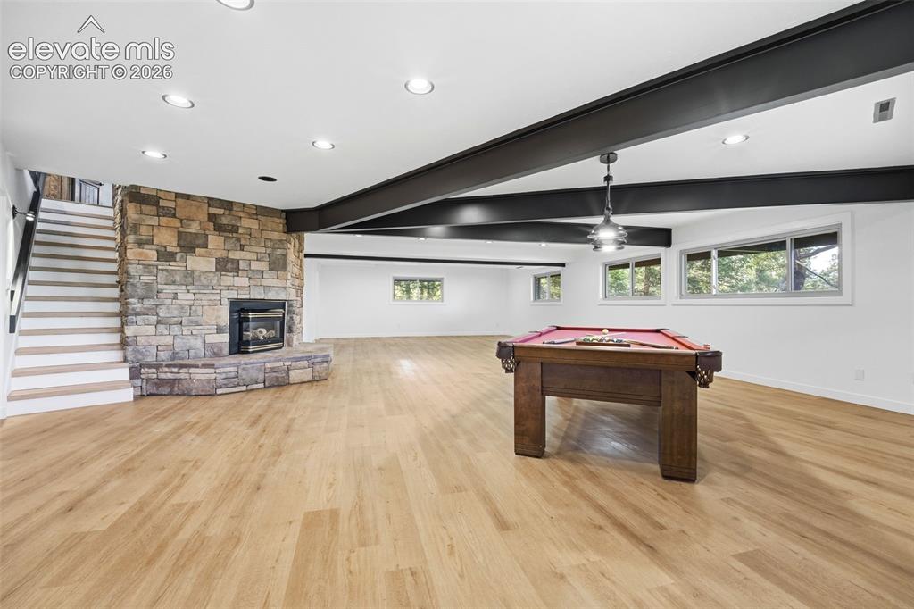 17 Pine Road Colorado Springs, CO 80906 - Photo 33 of 48 Spacious room featuring light wood-finish flooring, a stacked stone fireplace, exposed ceiling beams, recessed lighting, and multiple windows