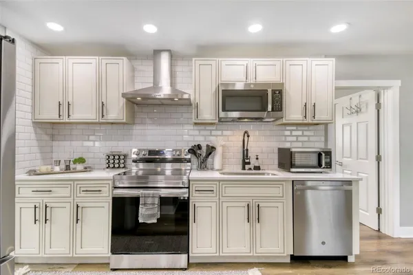 a kitchen with stainless steel appliances granite countertop white cabinets a sink a stove a refrigerator and a microwave