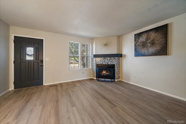 a view of an empty room with wooden floor fireplace and a window