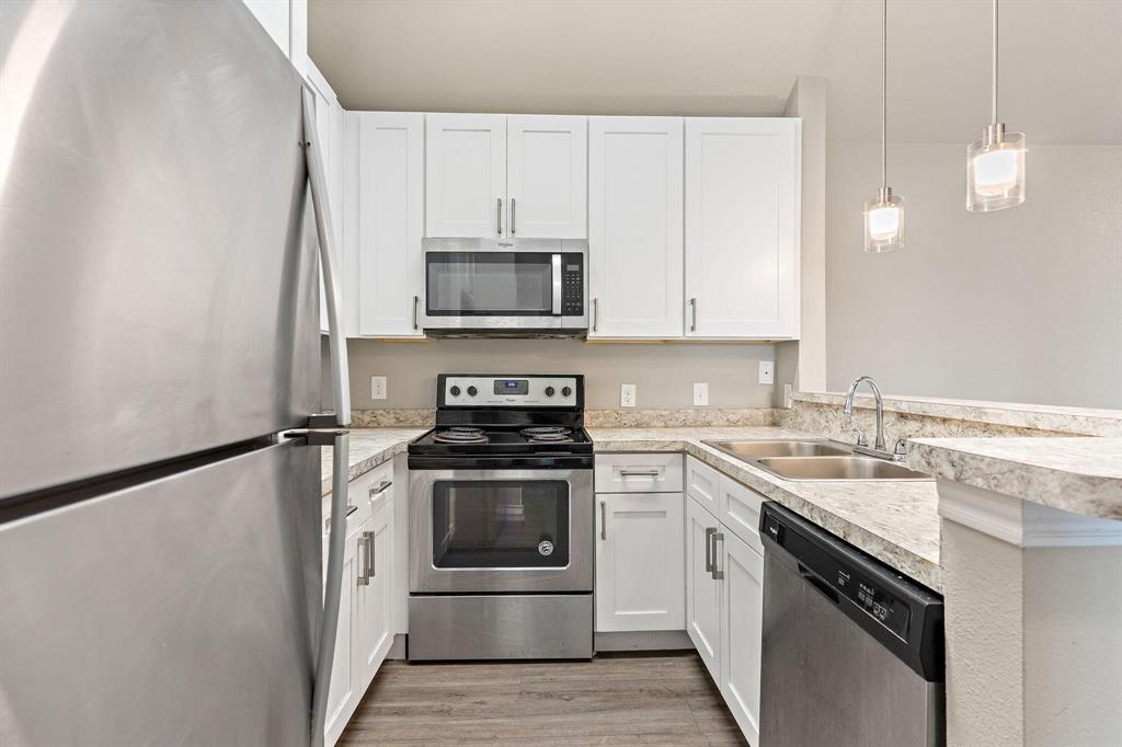6108 Abrams Road, Unit 521 Dallas, TX 75231 - Photo 14 of 20 Modern kitchen featuring white cabinetry, stainless steel appliances, wood-finish flooring, light-colored countertops, and pendant lighting
