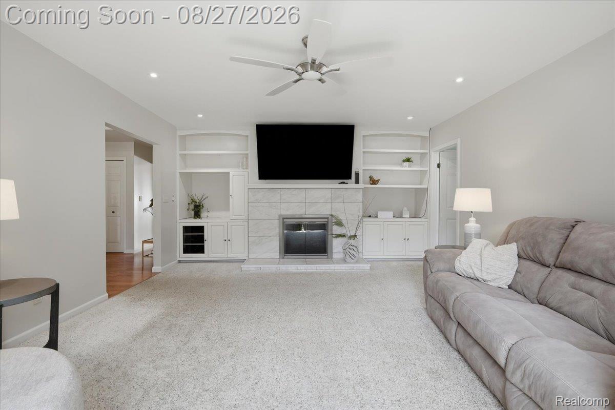 10100 Springtime Circle Clarkston, MI 48348 - Photo 11 of 73 Spacious living area featuring a central fireplace with a tiled surround, built-in shelving, a ceiling fan, and recessed lighting