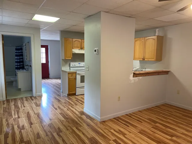 an empty room with wooden floor and a kitchen