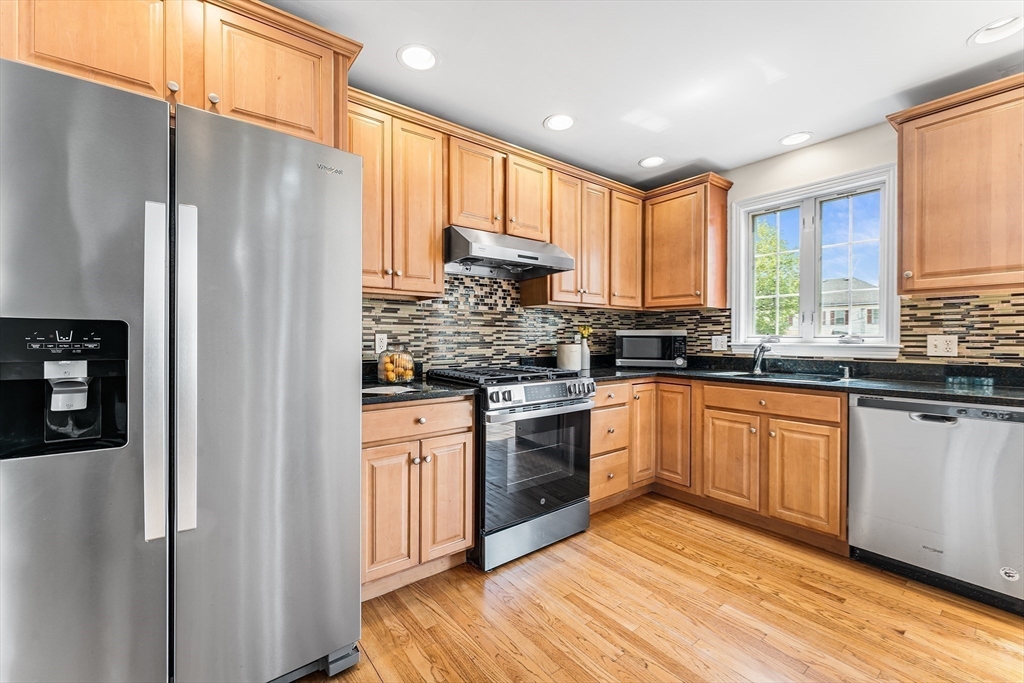 30 Russell Street, Unit 5 Waltham, MA 02453 - Photo 6 of 26 a kitchen with stainless steel appliances granite countertop a refrigerator a sink dishwasher a stove and white countertops with wooden floor