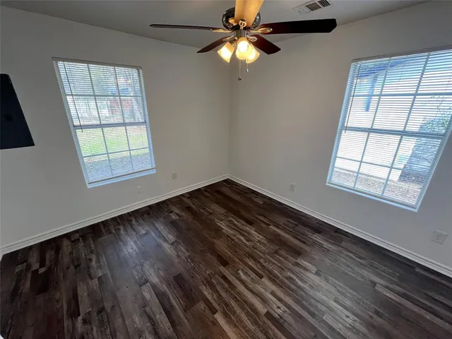 a view of an empty room with wooden floor and a ceiling fan