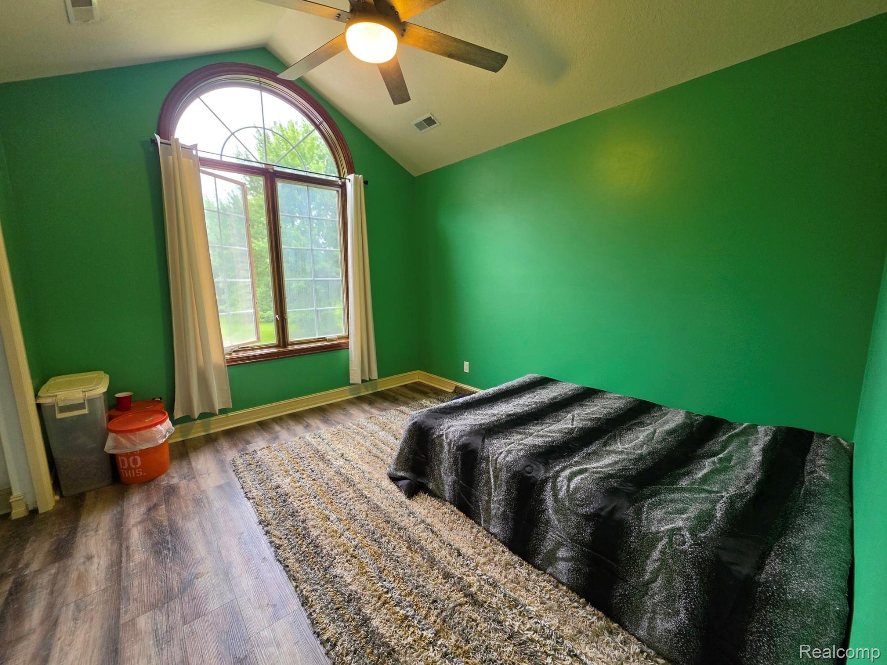 5150 West Carpenter Road Flint, MI 48504 - Photo 16 of 33 Room featuring a large arched window with a wooden frame, vaulted ceiling, wood-finish flooring, and a ceiling fan with integrated lighting