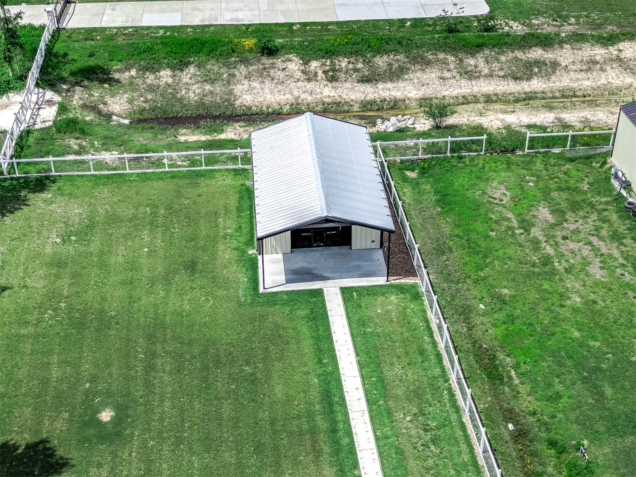 8032 Short Road Needville, TX 77461 - Photo 46 of 50 This aerial view highlights the fenced barn-style structure positioned on the expansive grassy portion of the property, offering additional versatility for storage, hobbies, equipment, recreational use, or future customization.