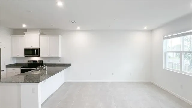 a kitchen with granite countertop a sink a stove a microwave a refrigerator and cabinets