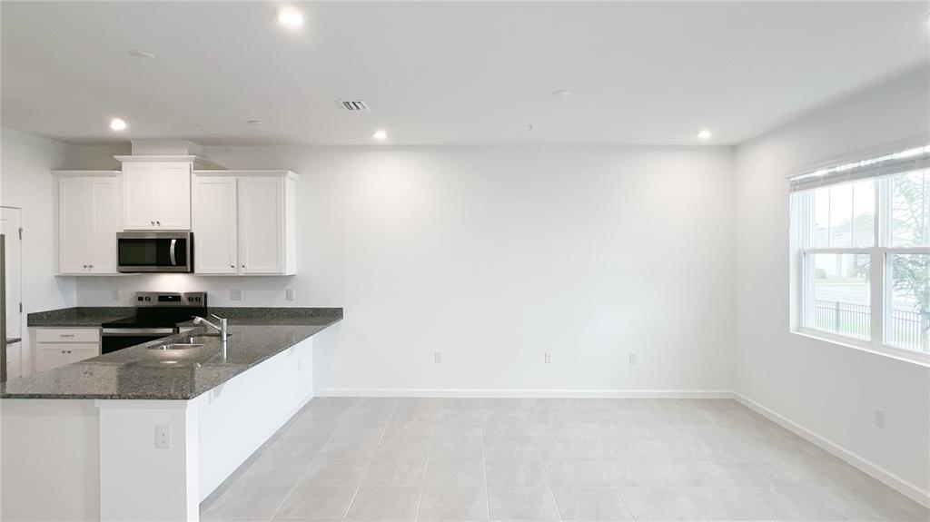 4268 Sadler Road Apopka, FL 32712 - Photo 9 of 28 a kitchen with granite countertop a sink a stove a microwave a refrigerator and cabinets