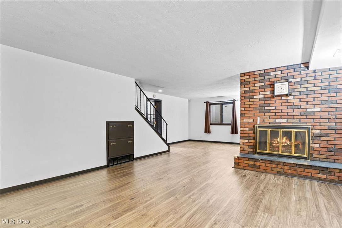 3863 Sourek Rd Extension Akron, OH 44333 - Photo 30 of 42 Unfurnished living room with a brick fireplace, stairway, light wood-style floors, and a textured ceiling
