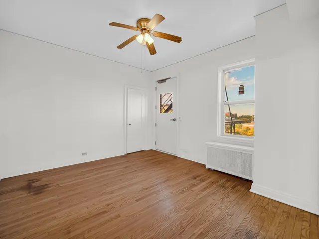 an empty room with wooden floor chandelier fan and windows