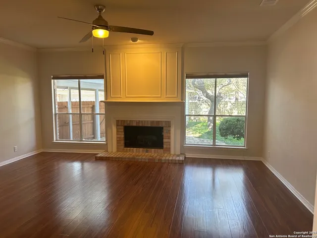 an empty room with wooden floor fireplace and windows