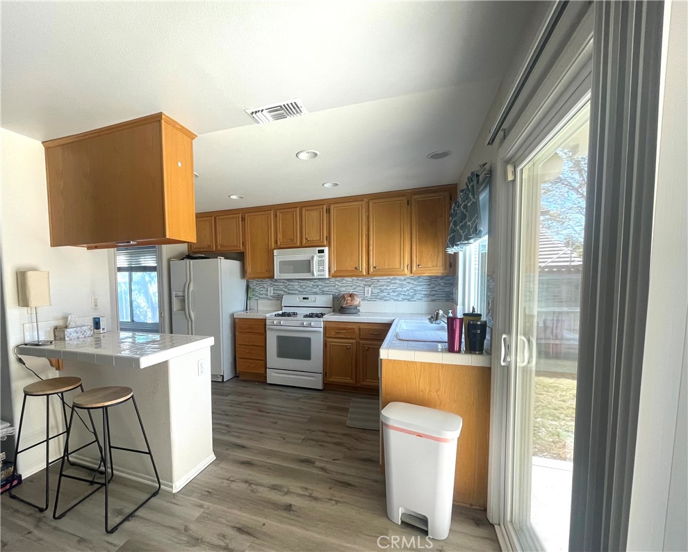 965 Hardwick Avenue Beaumont, CA 92223 - Photo 5 of 19 a kitchen with a table chairs refrigerator a sink dishwasher and a flat tv screen next to a window