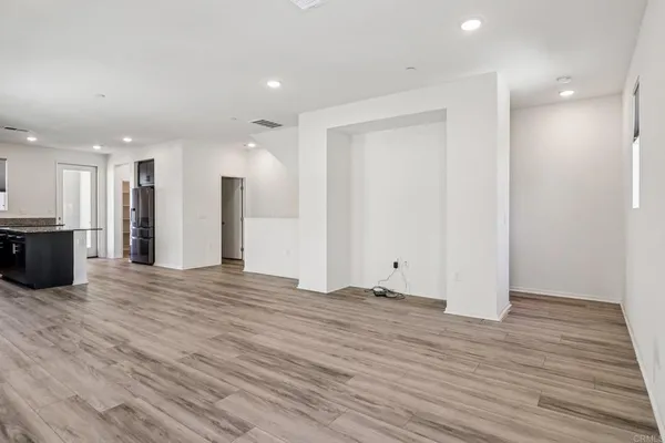 a view of an empty room with wooden floor and a kitchen