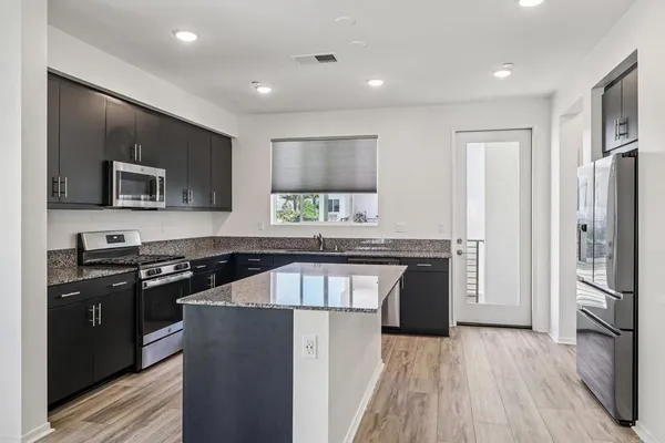 a kitchen with stainless steel appliances granite countertop a refrigerator a stove a sink dishwasher and a microwave oven with wooden floor