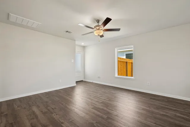 an empty room with wooden floor ceiling fan and windows