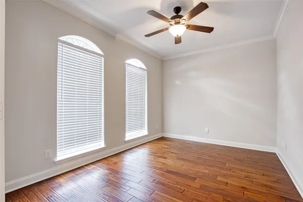 an empty room with wooden floor chandelier fan and windows