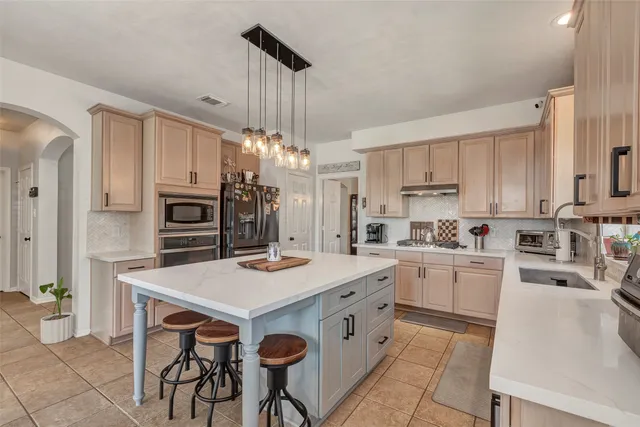 a open kitchen with stainless steel appliances granite countertop a stove top oven a refrigerator a sink dishwasher a dining table and chairs with wooden floor