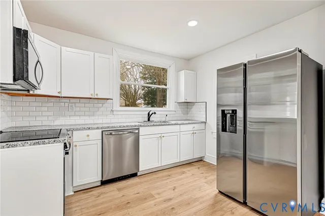 a kitchen with stainless steel appliances granite countertop a refrigerator a sink and white cabinets with wooden floor