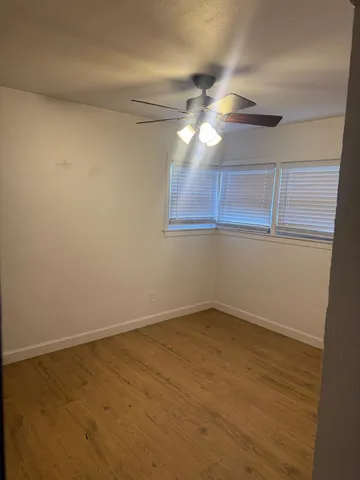 a view of an empty room with chandelier fan and wooden floor