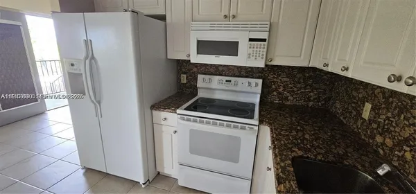 a kitchen with granite countertop white cabinets and refrigerator