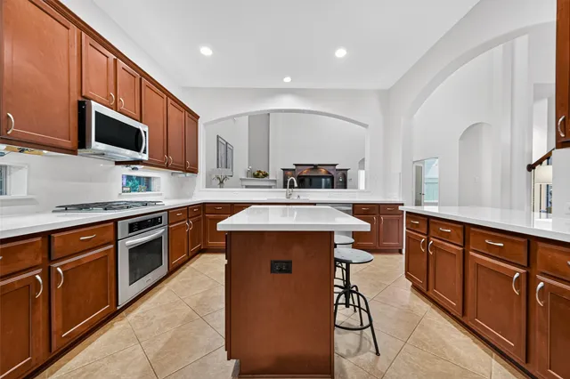 a kitchen with stainless steel appliances granite countertop wooden cabinets a sink a stove a refrigerator and island with wooden floor