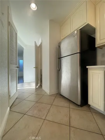 a view of a refrigerator in kitchen and an empty room in wooden floor
