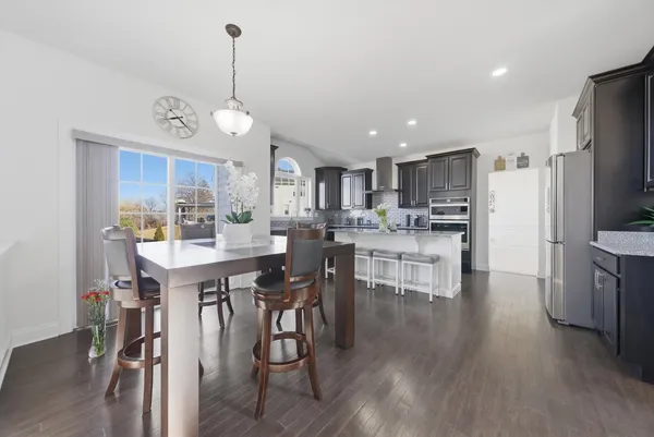 a kitchen with stainless steel appliances granite countertop a dining table chairs stove refrigerator and cabinets