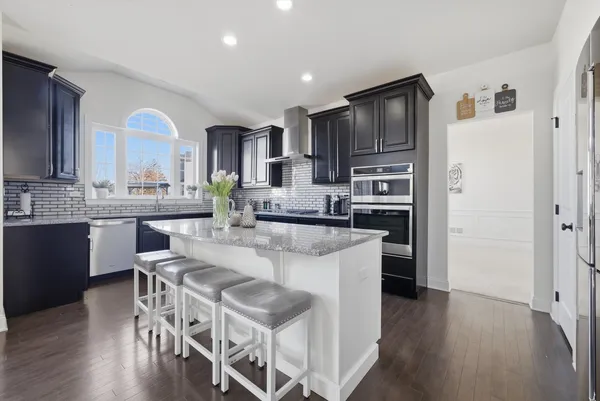 a kitchen with stainless steel appliances granite countertop a refrigerator a stove top oven a sink dishwasher and white cabinets with wooden floor