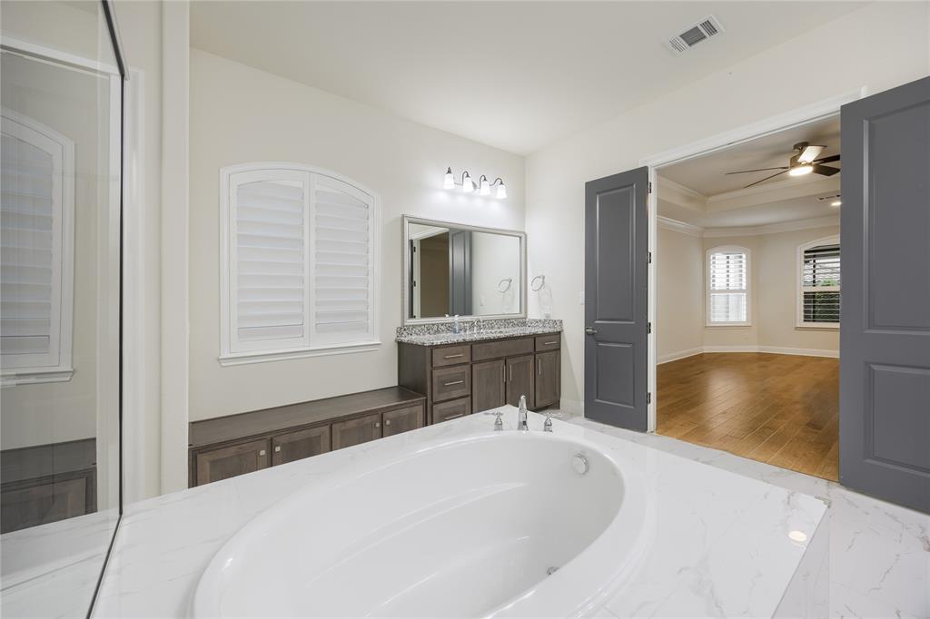 918 Sydney Lane Allen, TX 75013 - Photo 17 of 40 The bathroom features a built-in bathtub with a white marble surround, a vanity with granite countertops, and an arched window with white plantation shutters