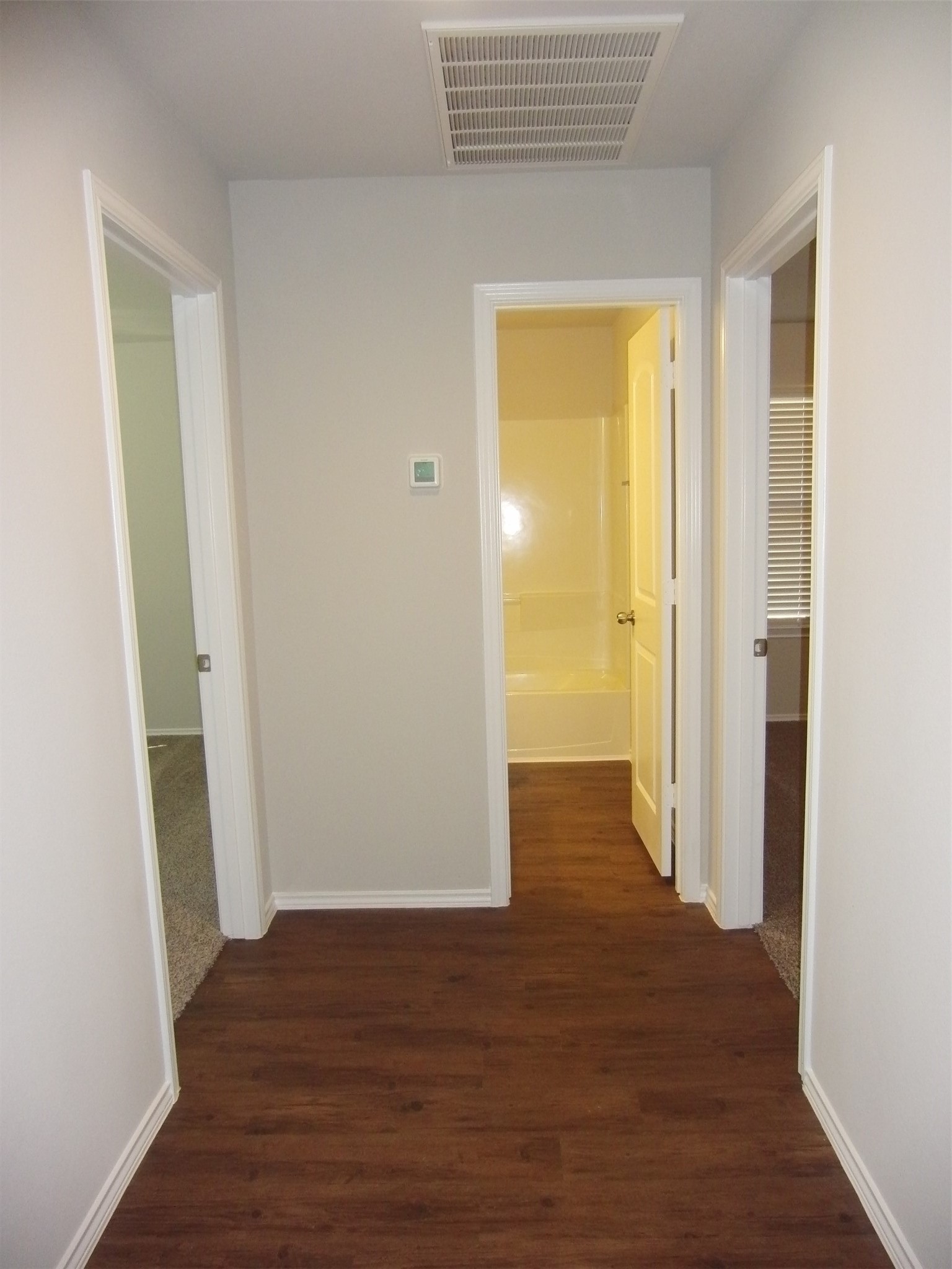 5522 Mesquite Oaks Trail Spring, TX 77389 - Photo 3 of 28 Hallway with wood flooring leading to three rooms. The central door opens to a bathroom with a bathtub, while the side doors lead to carpeted rooms.