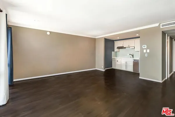 a view of an empty room with wooden floor and a kitchen