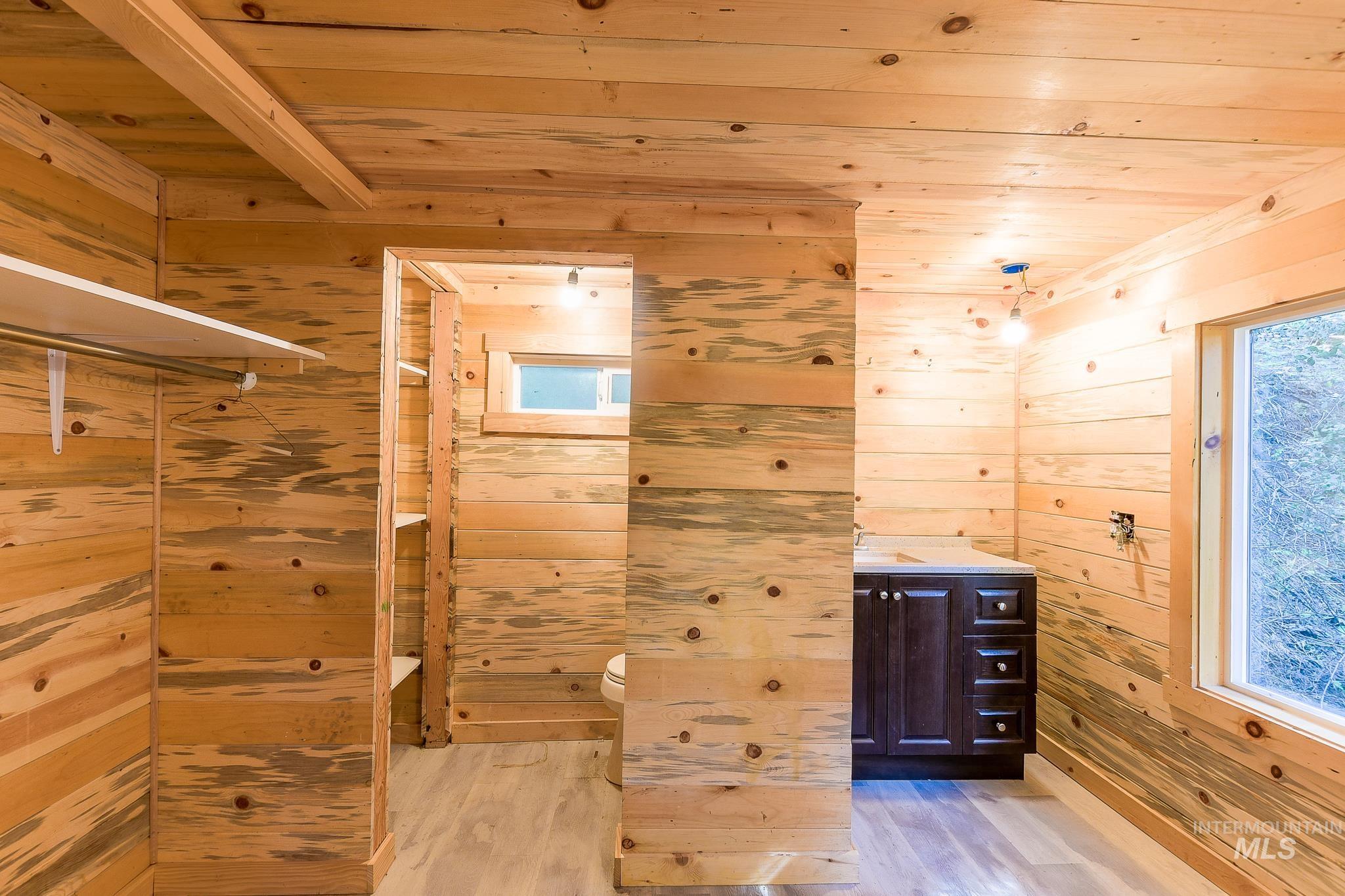 1206 Idlers Rest Road Moscow, ID 83843 - Photo 16 of 47 Interior space featuring natural wood paneling throughout, light wood-finish flooring, a built-in closet system with shelving and hanging rod, a dark wood vanity with a light countertop, and a window with exterior views