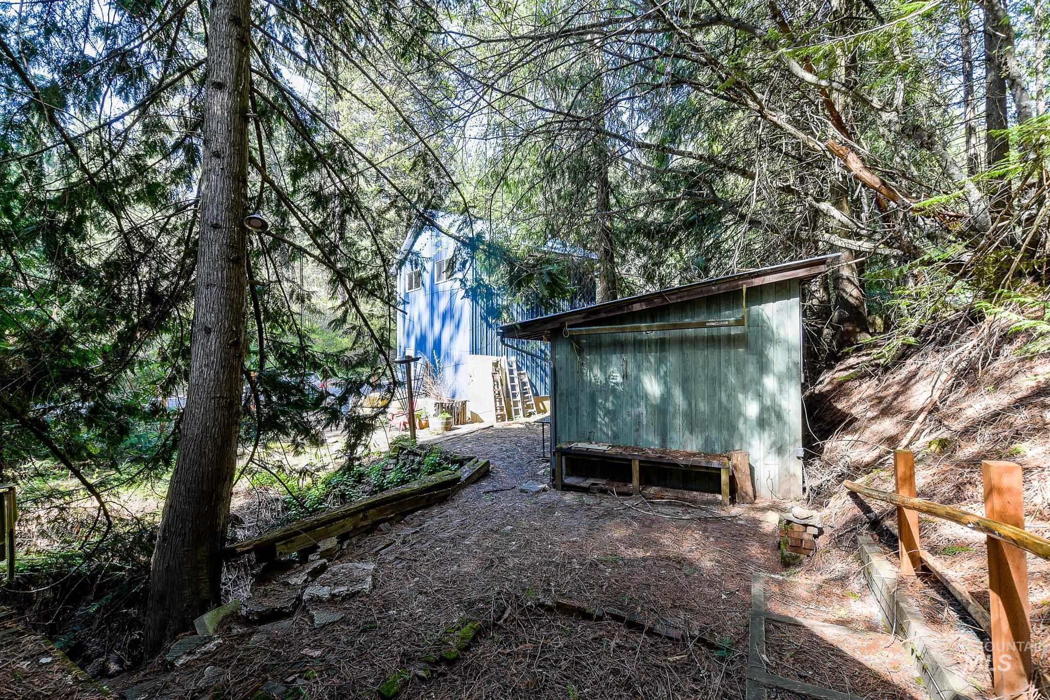 1206 Idlers Rest Road Moscow, ID 83843 - Photo 43 of 47 Wooded landscape featuring a light blue structure, a rustic green shed with a sloped roof, and natural wood handrails