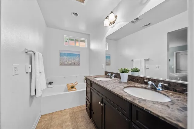 a bathroom with a granite countertop double vanity sink a mirror and a bathtub