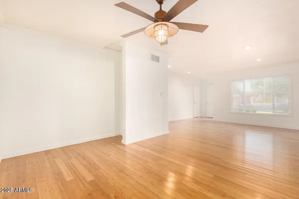 an empty room with wooden floor fan and windows