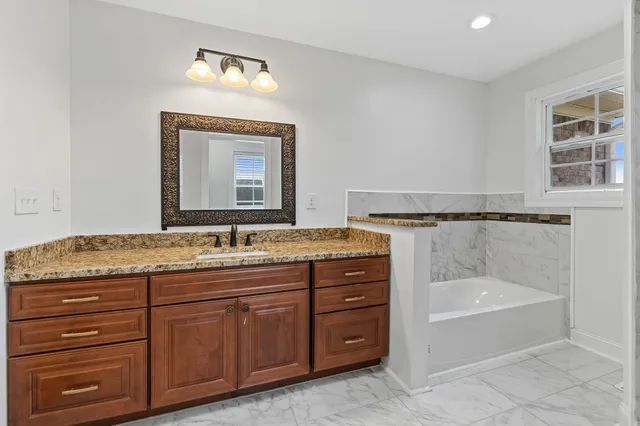 a bathroom with a granite countertop bathtub a sink and a mirror